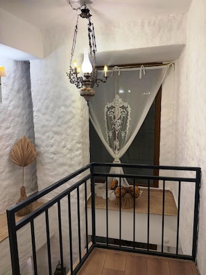 Una escalera con barandilla negra, pared blanca y un candelabro decorativo.