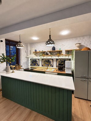 A kitchen with a central island, wooden shelves, a refrigerator, and pendant lighting. - Urla Lime Hotel (Urla)