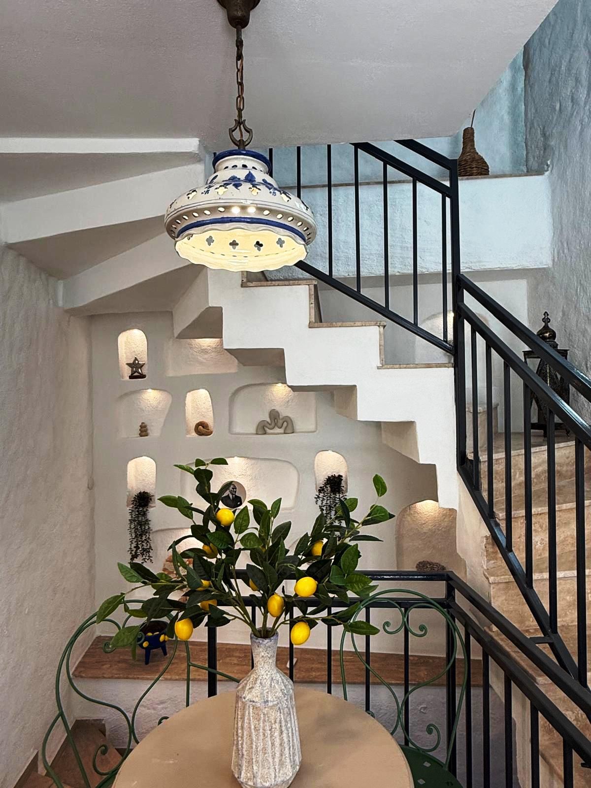 A staircase with a black railing, a hanging light fixture, and a table with a vase of lemons.