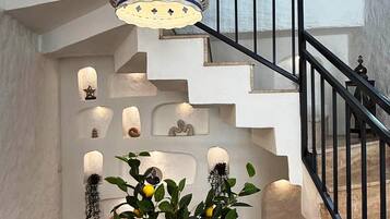 A staircase with a black railing, a hanging light fixture, and a table with a vase of lemons.