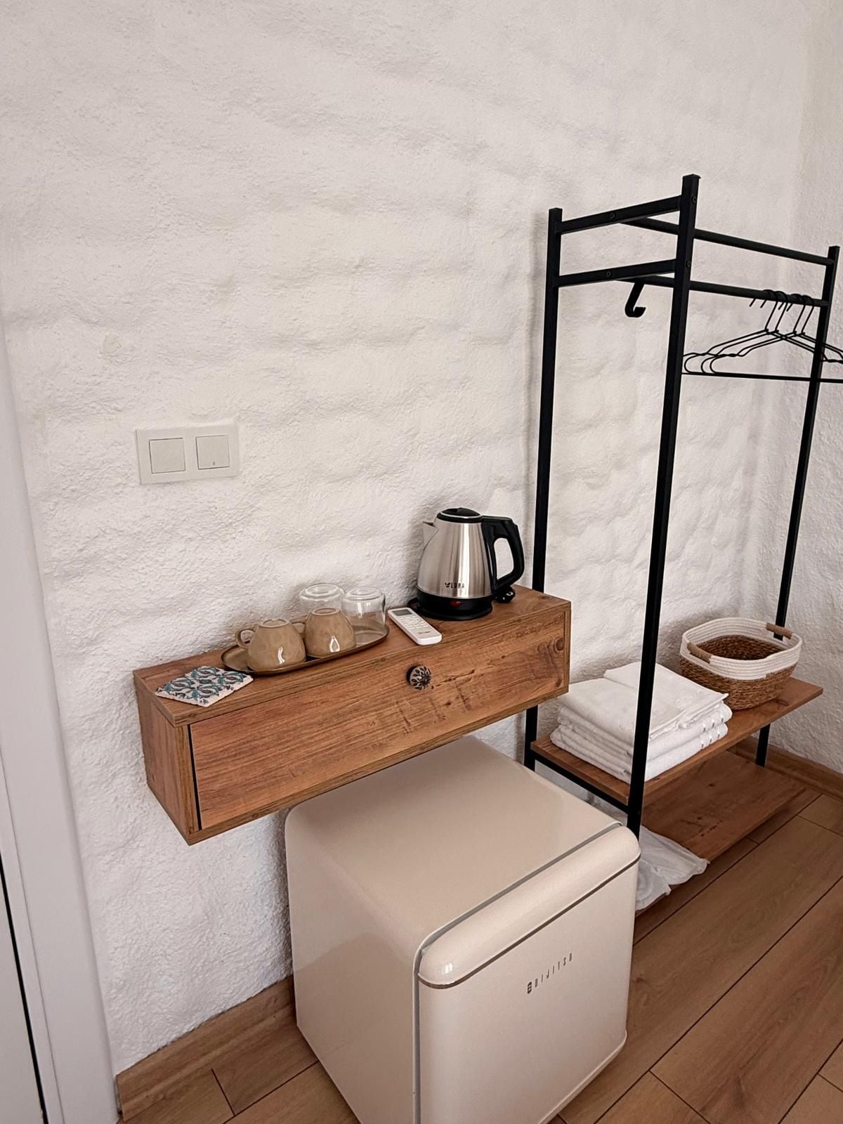 Une petite cuisine équipée comprenant un réfrigérateur, un plan de travail en bois, une bouilloire et un égouttoir.