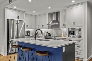 A modern kitchen with a large island, stainless steel appliances, and white cabinetry. - The Bluebird Suite - Mountain Views - Hot Tub - 2BR (Canmore)