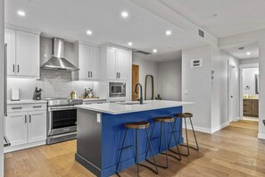 A modern kitchen with white cabinetry, stainless steel appliances, and a blue accent wall. - The Bluebird Suite - Mountain Views - Hot Tub - 2BR (Canmore)
