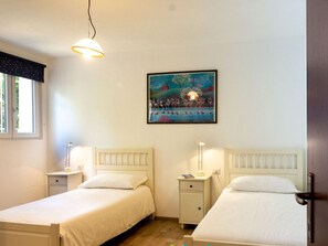 A bedroom with two beds, a nightstand with a lamp, a painting on the wall, and a window with curtains. - Holiday Apartment With 2 Bedrooms (Tremosine)