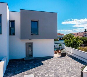 A modern building with a flat roof, a small entrance, and a pool area with lounge chairs. - Holiday home Val (Šibenik)