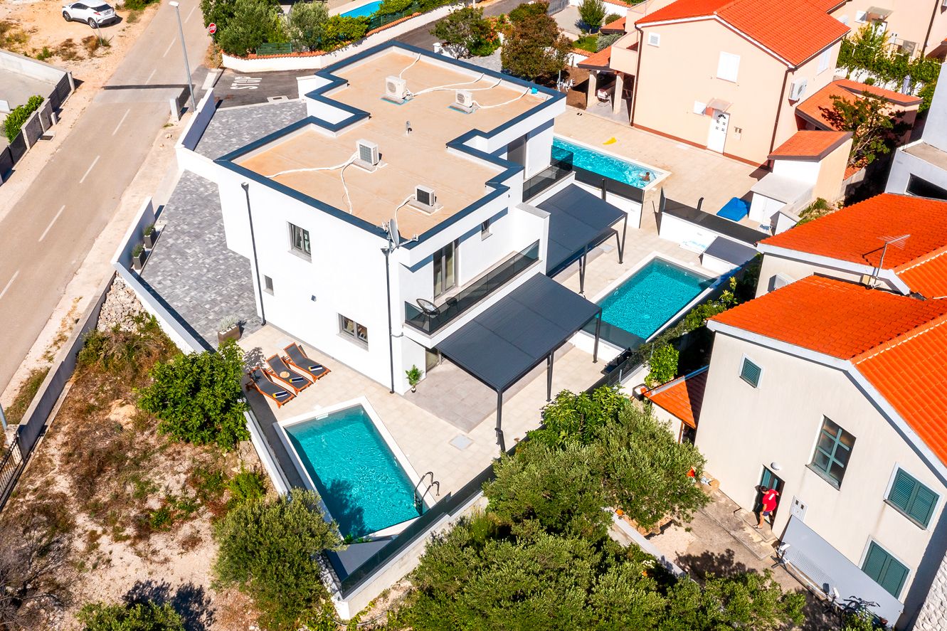 A modern two-story building with a rooftop terrace, a swimming pool, and a covered outdoor seating area.