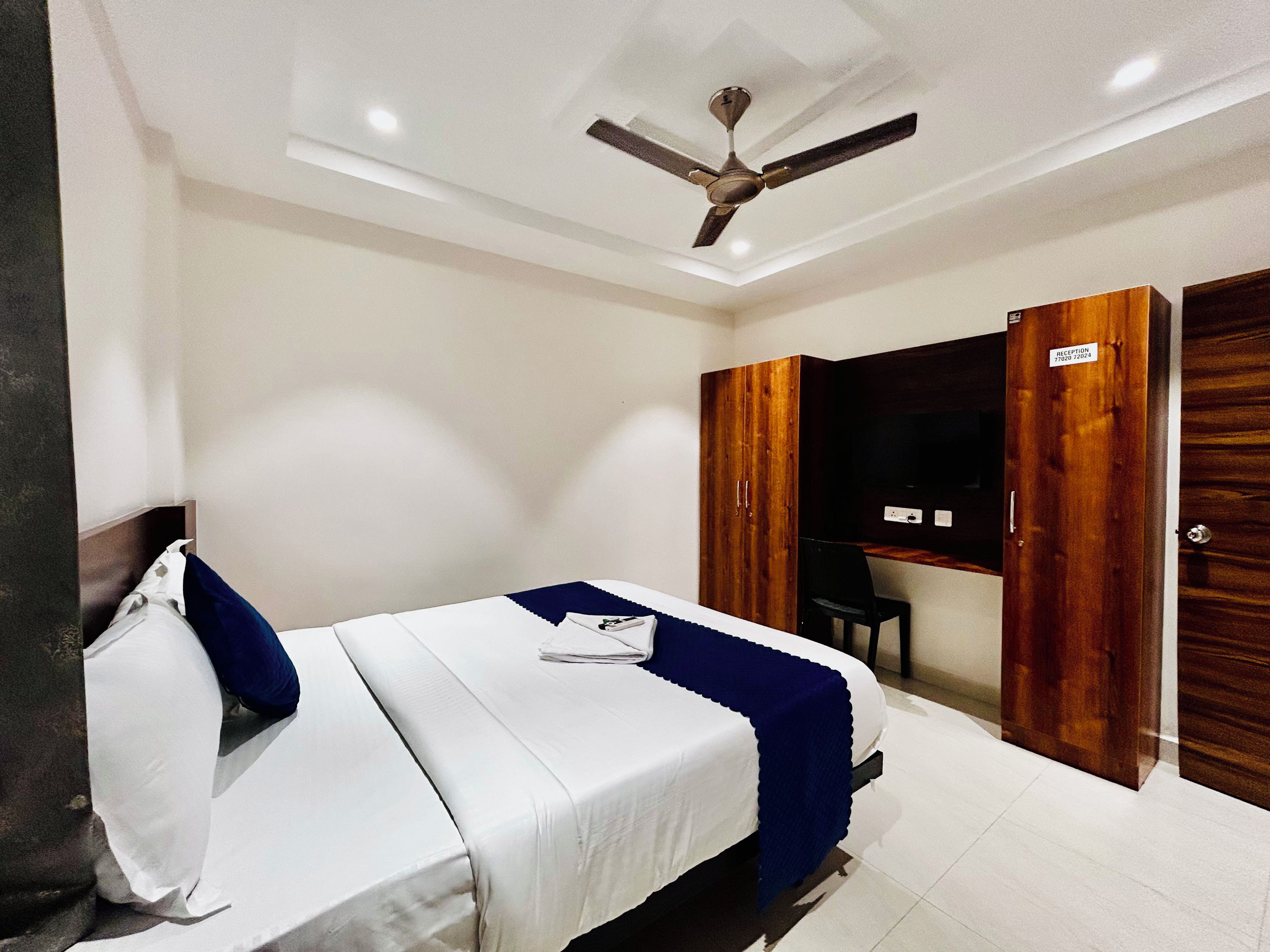 Habitación de hotel con cama, escritorio, armario y ventilador de techo.