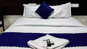 A neatly made bed with white linens, a blue pillow, and a folded towel with a remote control and a card on it. - Orion Signature Hotel  (Hyderabad)
