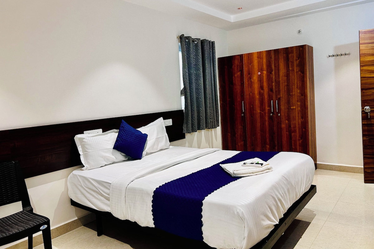A hotel room with a bed, a chair, a wardrobe, and a ceiling fan.