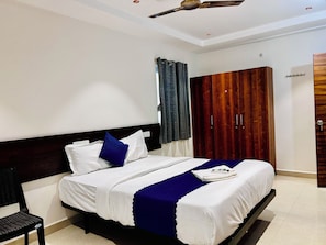 A hotel room with a bed, a chair, a wardrobe, and a ceiling fan. - Orion Signature Hotel  (Hyderabad)