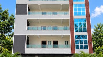 Um edifício de vários andares com telhado plano, varandas e entrada com ladrilhos xadrez.