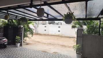 Un espacio al aire libre techado con macetas colgantes, suelo de baldosas y vista a una calle residencial.
