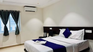A hotel room with a bed, a ceiling fan, an air conditioning unit, a nightstand, and a window with curtains. - Orion Signature Hotel  (Hyderabad)
