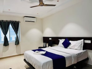 A hotel room with a bed, a ceiling fan, an air conditioning unit, a nightstand, and a window with curtains. - Orion Signature Hotel  (Hyderabad)