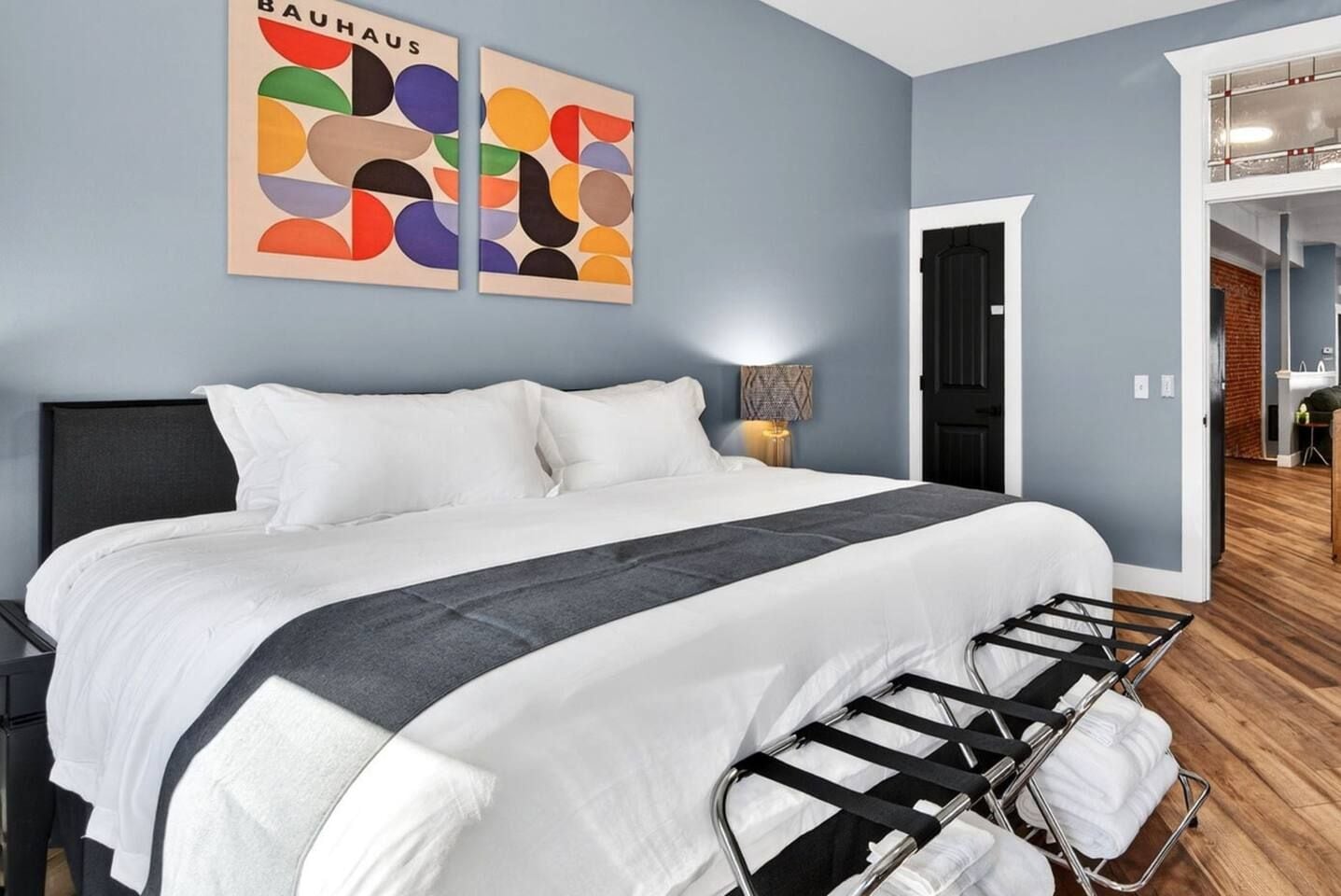 Una habitación de hotel con una cama, una mesita de noche, una lámpara y una pared decorada con arte abstracto.