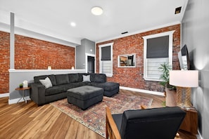 Una sala moderna con pared de ladrillo, un sofá modular, una mesita auxiliar y un ventanal grande.