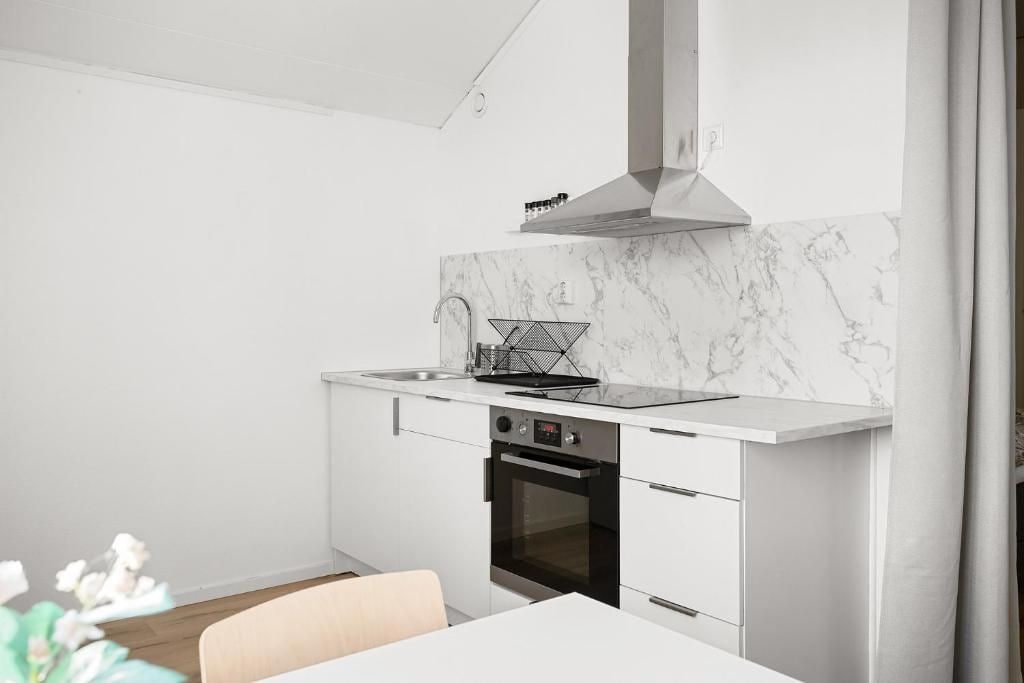 Une cuisine moderne avec des meubles blancs, un pare-feu en marbre et un four encastré.
