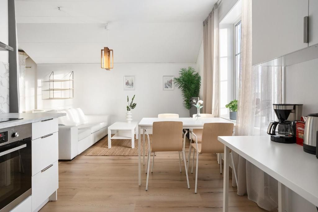 A modern kitchen with white cabinetry, a dining area with a white table and chairs, and a large window providing natural light.