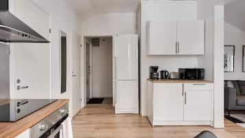 Cocina compacta con armarios blancos, microondas y cafetera sobre la encimera.