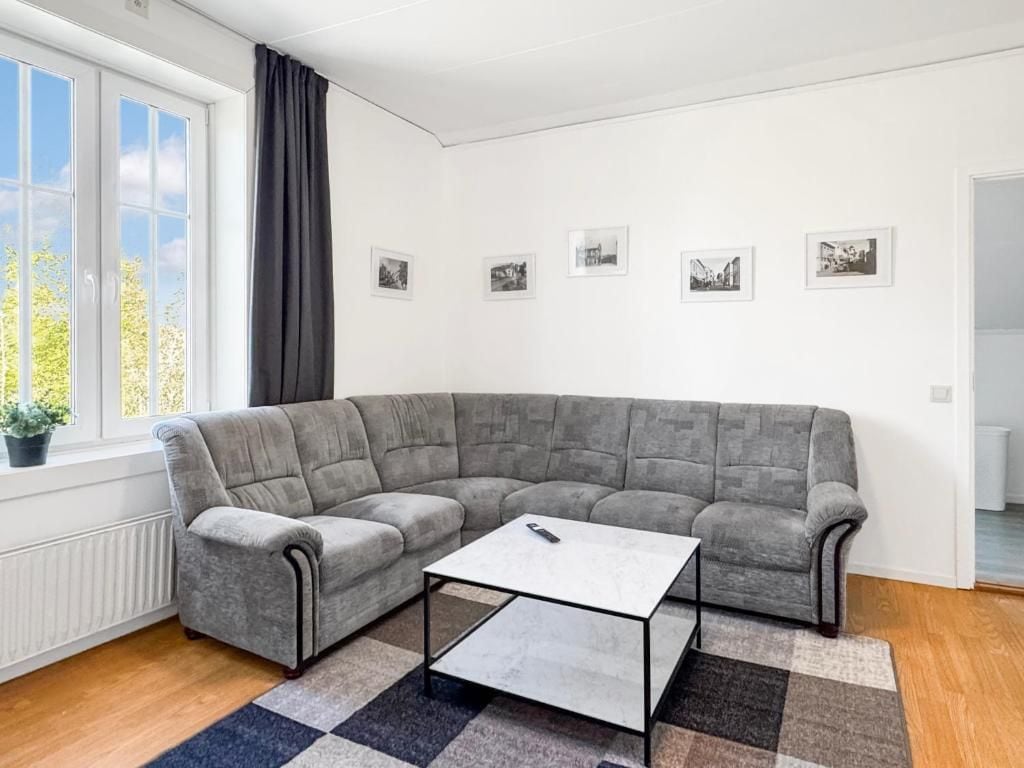 Un salon moderne avec un canapé d’angle gris, une table basse blanche et un tapis à motifs.