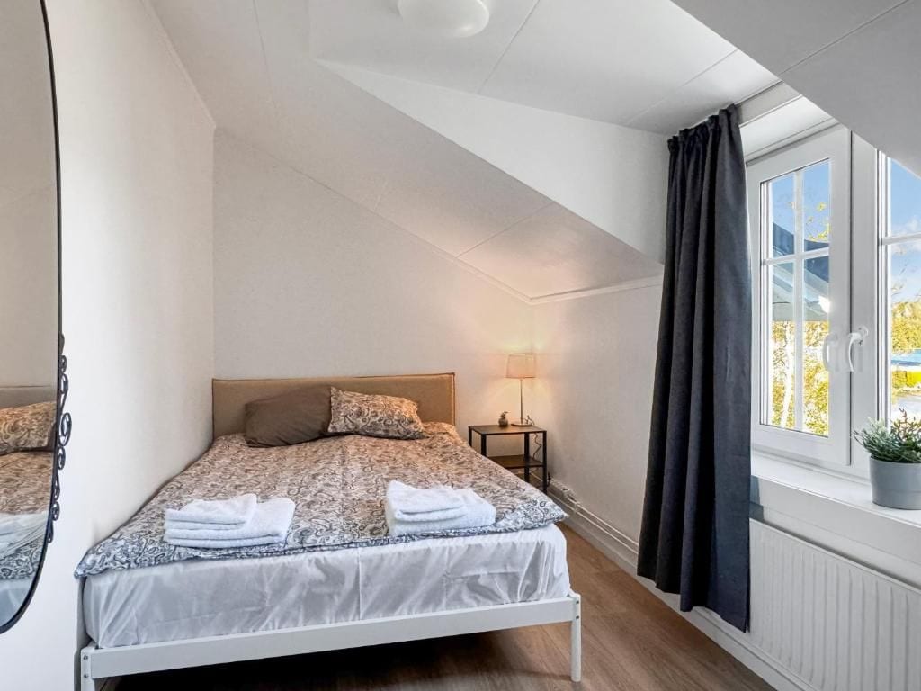 Ett sovrum med en säng, ett nattduksbord, en lampa, ett fönster och gardiner.