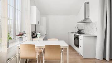 Une cuisine moderne avec un plan de travail blanc, une cuisinière et un évier. On y trouve une table à manger avec des chaises et une fenêtre avec des rideaux.