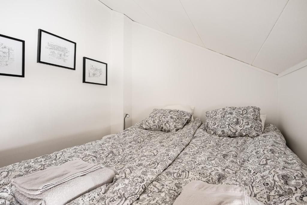 A bedroom with a bed, two pillows, a blanket, and three framed pictures on the wall.