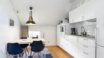 A compact kitchen with white cabinets, a microwave, and a coffee maker. There is a dining table with chairs and a rug.