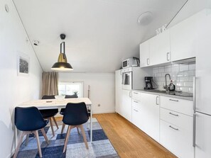 A compact kitchen with white cabinets, a microwave, and a coffee maker. There is a dining table with chairs and a rug.