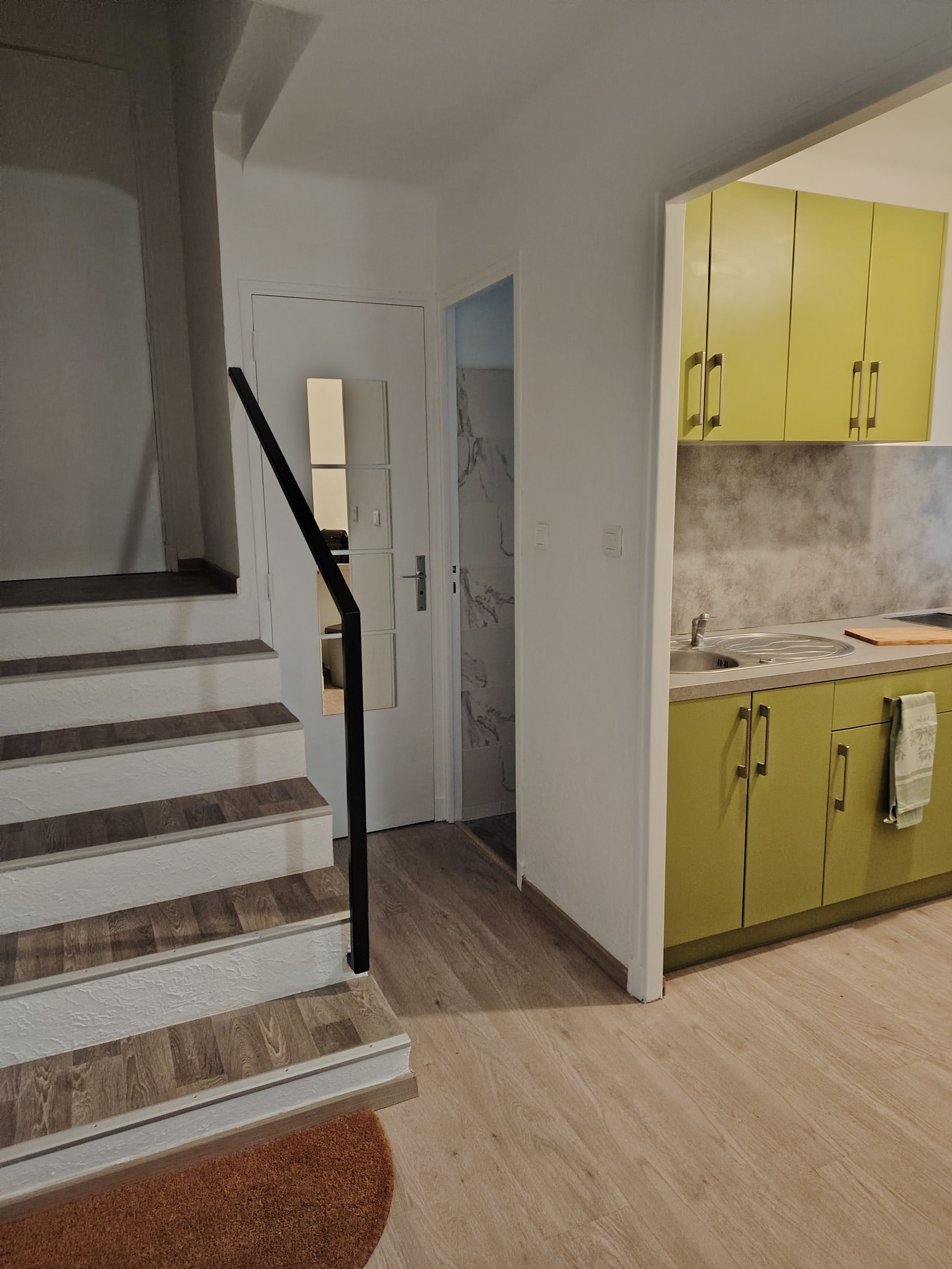 Une cuisine moderne avec des meubles de couleur verte, un pare-feu en marbre et un escalier en bois doté d’une rampe noire.
