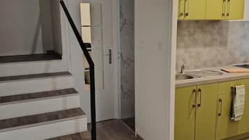 Une cuisine moderne avec des meubles de couleur verte, un pare-feu en marbre et un escalier en bois doté d’une rampe noire.