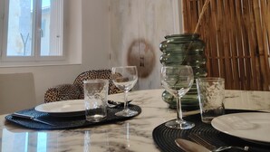 A dining area with a ceiling fan, a table set with plates, glasses, and cutlery, and a window with blinds. - Apartment in downtown Toulon, between the port and the train station (Toulon)