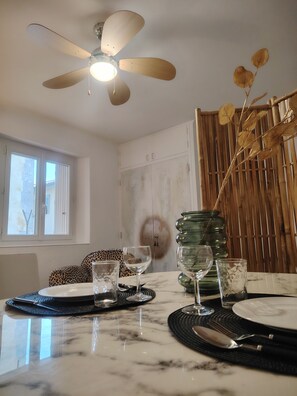 A dining area with a ceiling fan, a table set with plates, glasses, and cutlery, and a window with blinds. - Apartment in downtown Toulon, between the port and the train station (Toulon)