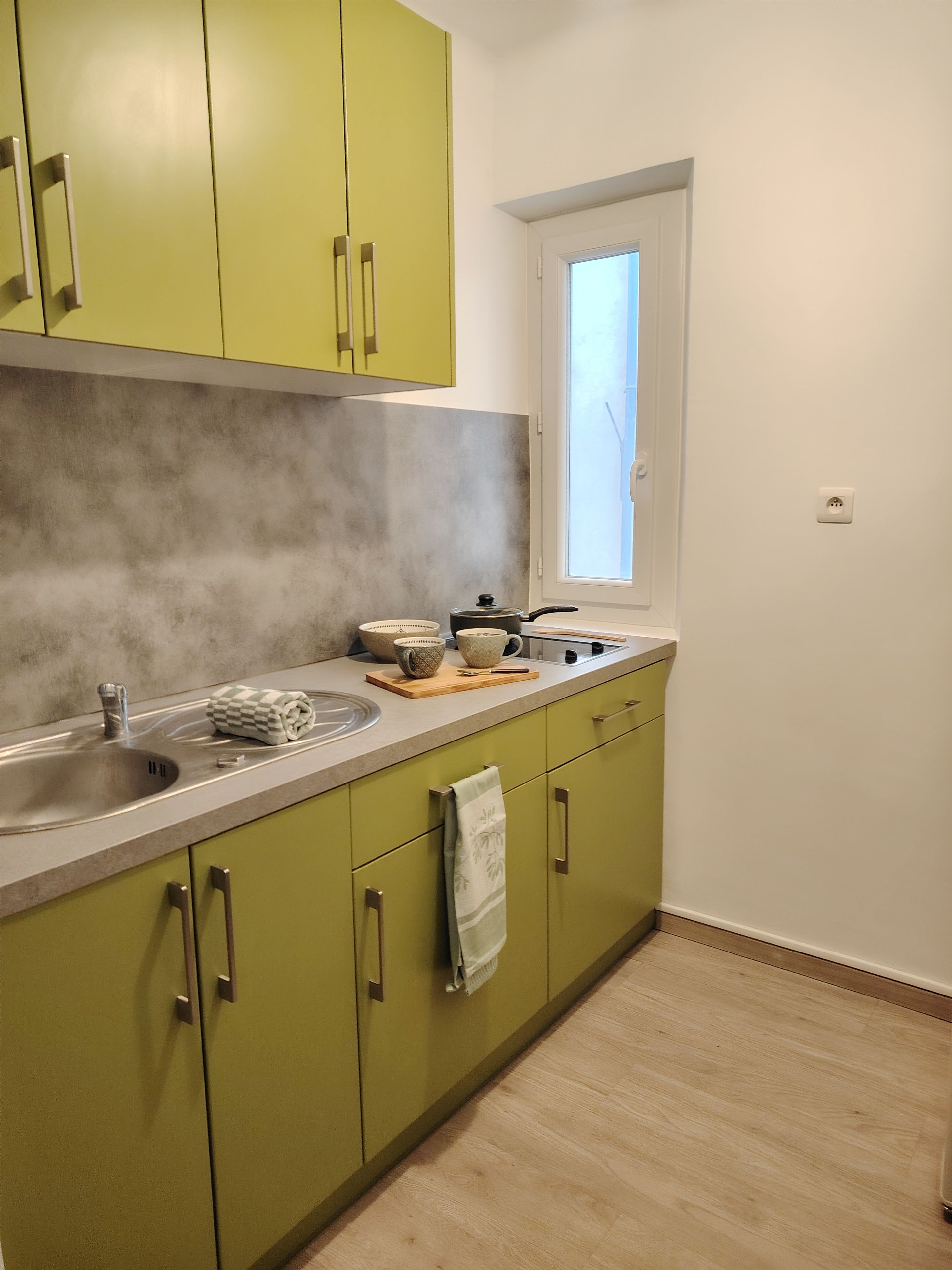 A kitchen with green cabinets, a sink, and a window.