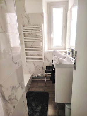 A bathroom with a white bathtub, a white sink with a mirror, and a black rug on the floor. - Apartment in downtown Toulon, between the port and the train station (Toulon)