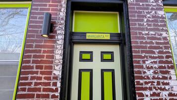Een gevel van een gebouw met een bakstenen buitenkant, een deur in groen en zwart, en een bord boven de deur met de tekst 'MARGARITA WAY'.
