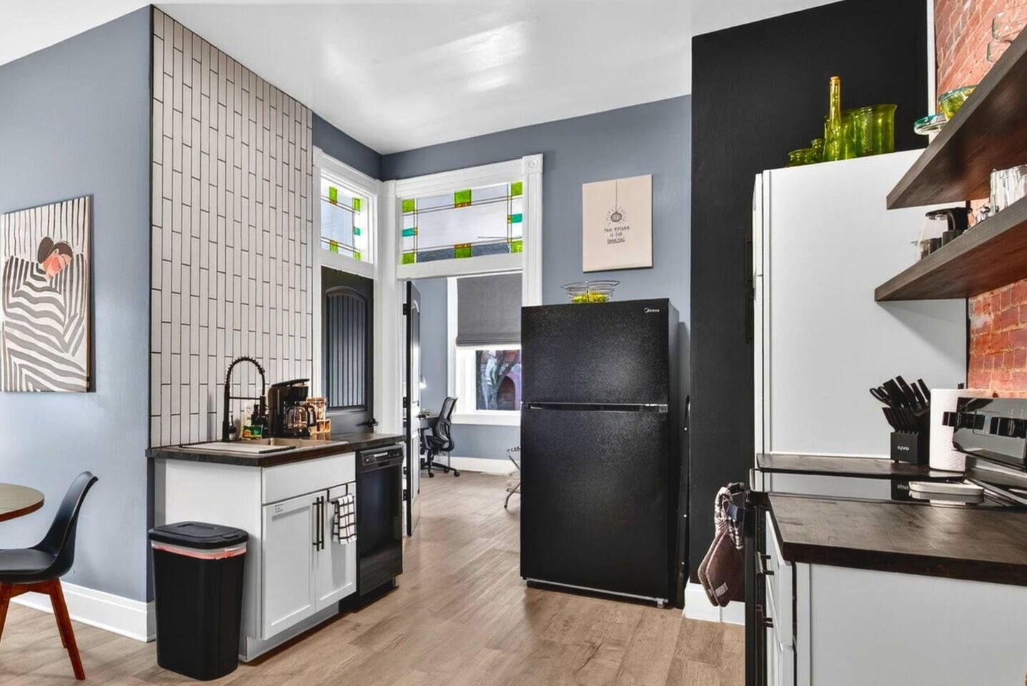 Een moderne keuken met een zwarte koelkast, witte kastjes en een houten vloer.
