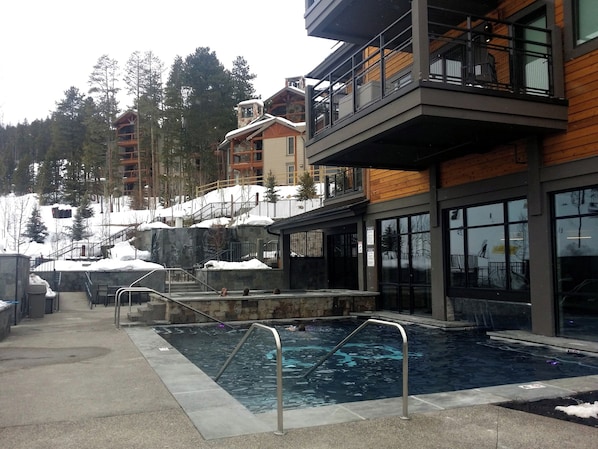 Uma área de piscina com deck de pedra, grades de metal e vista para uma paisagem montanhosa.