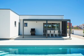 A modern outdoor dining area with a pool in the foreground. - Villa Pure (Šibenik)