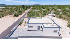 A modern building with a flat roof, a paved driveway, and a boat docked nearby. - Villa Pure (Šibenik)