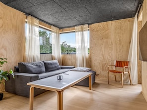 Ein modernes Wohnzimmer mit einer Couch, einem Couchtisch, einem Sessel und großen Fenstern.