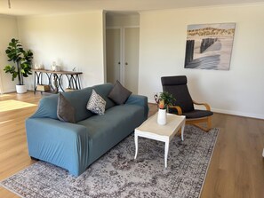 A living room with a sofa, a coffee table, a chair, a plant, and a painting on the wall.