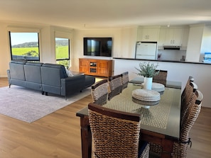 A modern living room with a sofa, a dining table with chairs, a kitchen area with cabinets and a TV.