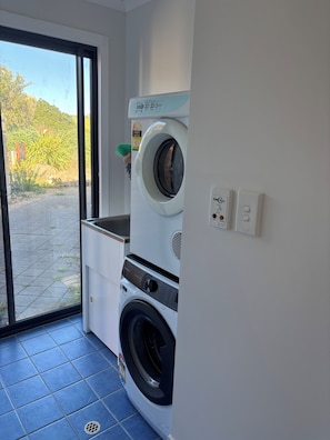 A laundry room with a front-loading washing machine, a dryer, and a small window with a view of greenery outside.