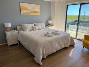 A bedroom with a large bed, two bedside tables, a nightstand, a window with a view of a grassy field, and a yellow chair.