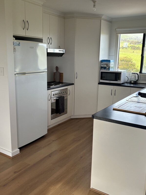 A modern kitchen with white cabinetry, a built-in oven, a microwave, and a kettle on the countertop.
