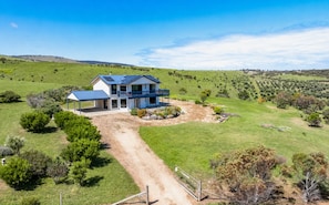A two-story house with a covered patio and solar panels, surrounded by a lush green landscape.