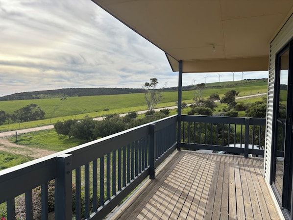 A wooden deck with a view of a green field and wind turbines in the distance.