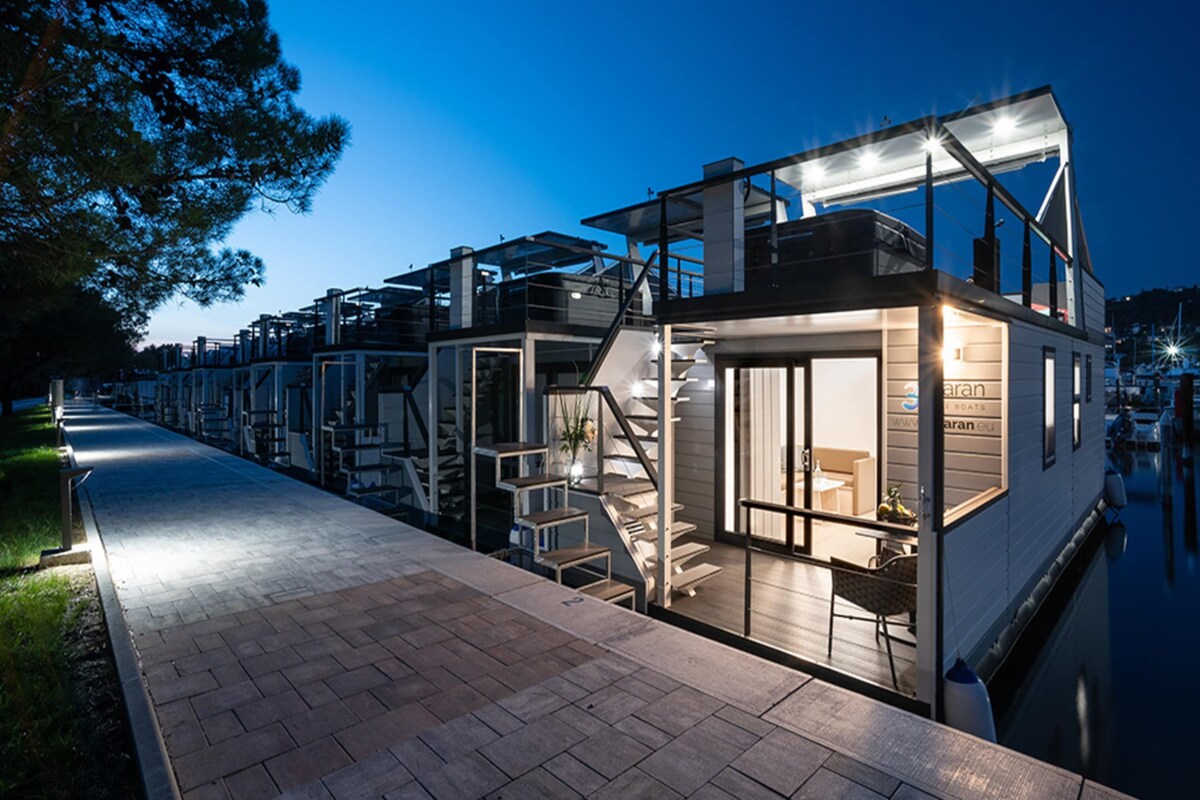 A waterfront property with a glass-enclosed structure, outdoor seating, and a staircase leading to the upper level.