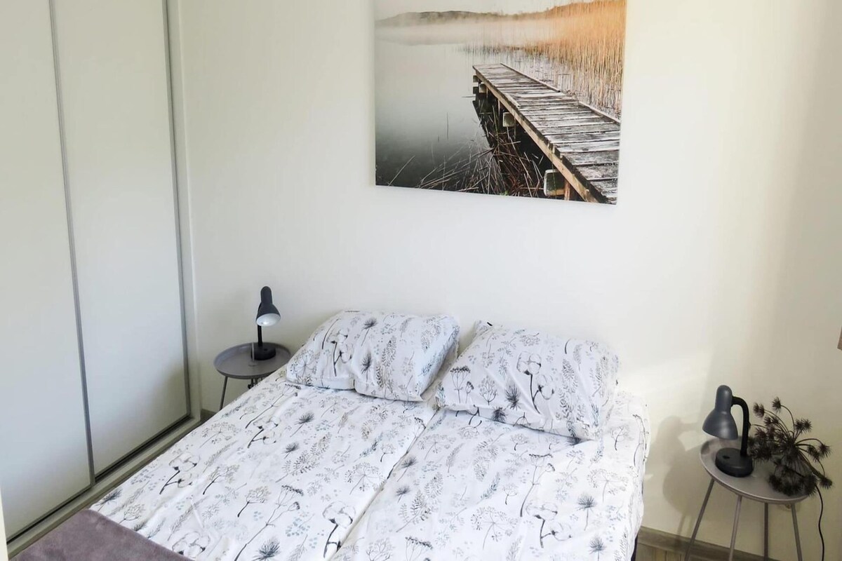 Ein Schlafzimmer mit einem Bett, einem Nachttisch, einer Lampe und einem Wandbild.